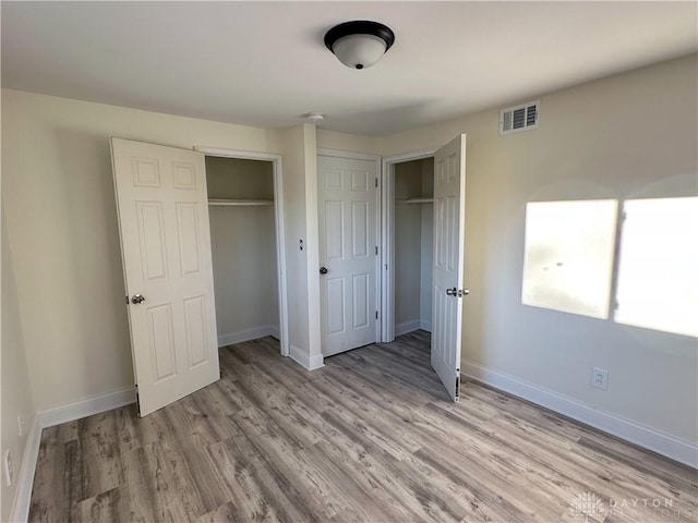 unfurnished bedroom featuring light hardwood / wood-style flooring and multiple closets