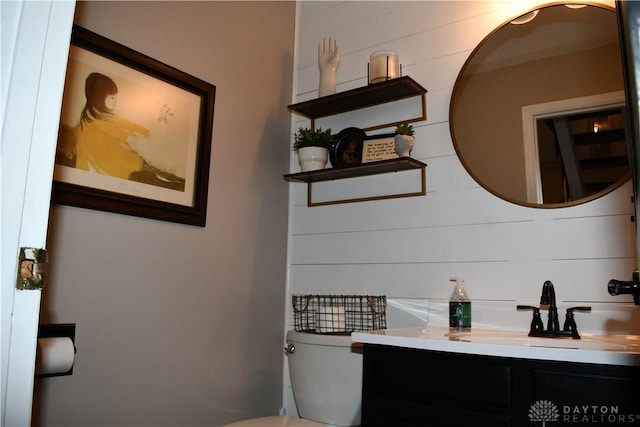 bathroom with wooden walls, vanity, and toilet