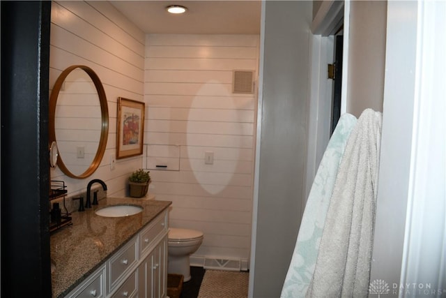 bathroom featuring vanity, toilet, and wooden walls