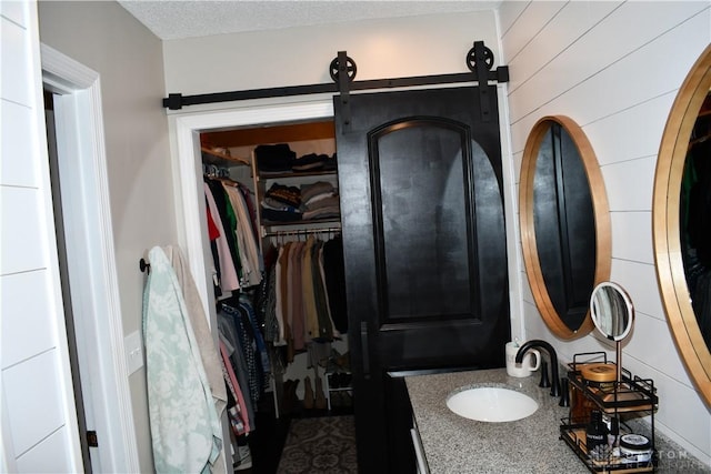 bathroom featuring a textured ceiling, vanity, and wood walls