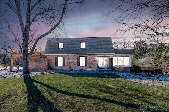 rear view of property with mansard roof, roof with shingles, a yard, french doors, and brick siding