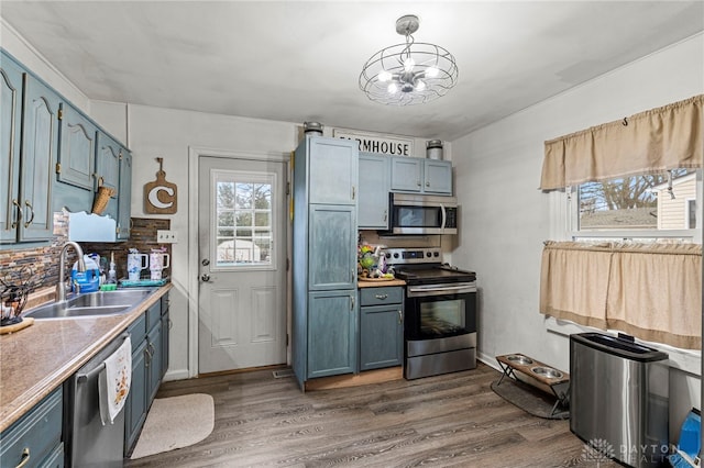 kitchen with appliances with stainless steel finishes, sink, blue cabinetry, decorative light fixtures, and dark hardwood / wood-style floors