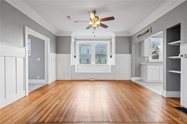 unfurnished living room with hardwood / wood-style flooring, built in features, ceiling fan, and ornamental molding