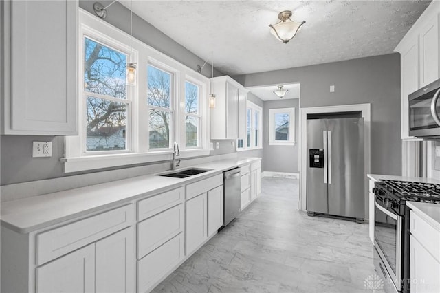 kitchen featuring hanging light fixtures, sink, a textured ceiling, appliances with stainless steel finishes, and white cabinetry