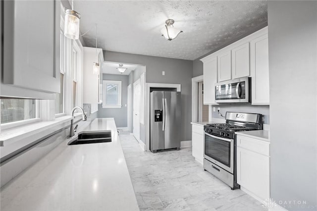 kitchen featuring a textured ceiling, stainless steel appliances, sink, pendant lighting, and white cabinetry