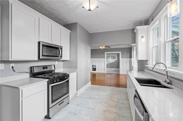 kitchen with appliances with stainless steel finishes, ceiling fan, sink, decorative light fixtures, and white cabinetry