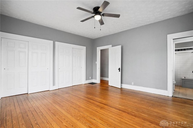 unfurnished bedroom with ensuite bathroom, ceiling fan, a textured ceiling, and two closets