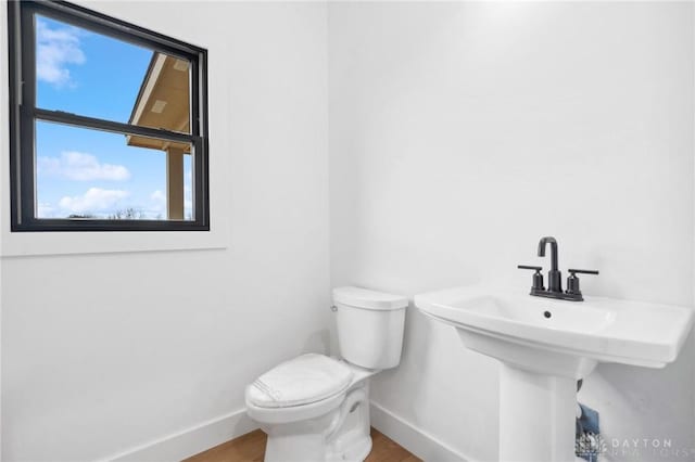 bathroom with toilet, baseboards, a wealth of natural light, and wood finished floors