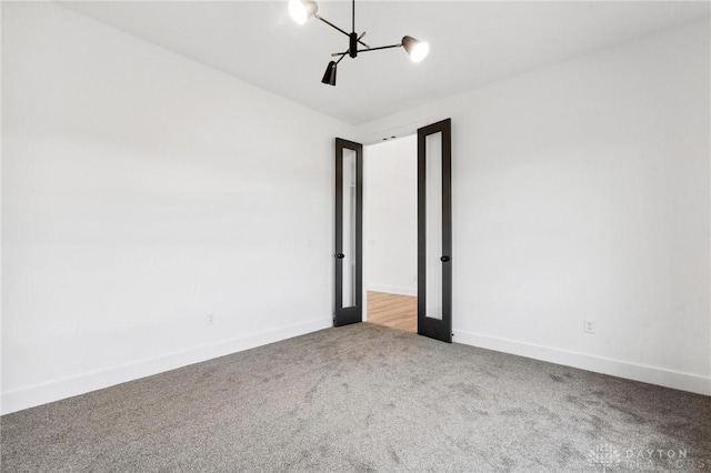 carpeted spare room featuring baseboards and a notable chandelier
