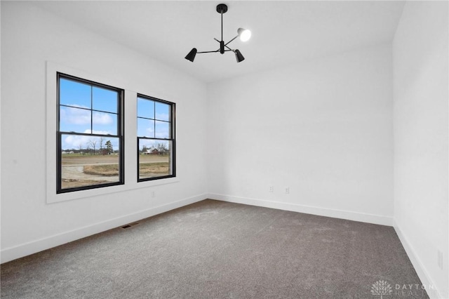 spare room featuring an inviting chandelier, baseboards, dark colored carpet, and visible vents
