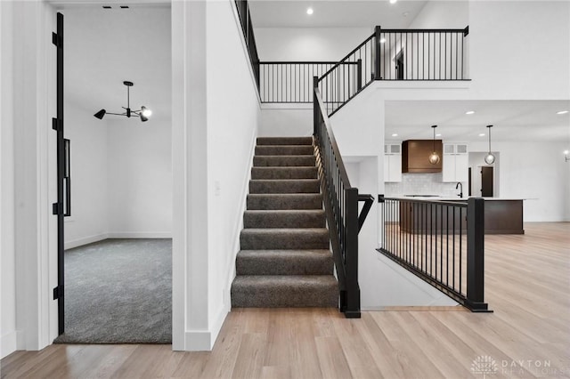 staircase featuring baseboards, a high ceiling, recessed lighting, and wood finished floors