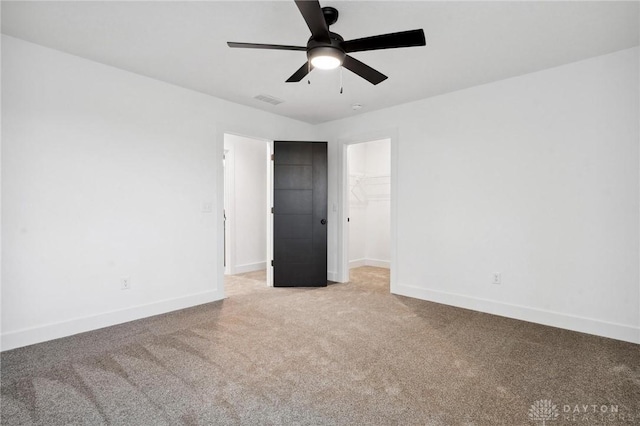 unfurnished bedroom featuring light colored carpet, baseboards, a walk in closet, and visible vents