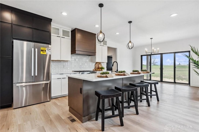 kitchen with a kitchen breakfast bar, tasteful backsplash, light wood-type flooring, light countertops, and stainless steel fridge