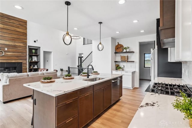 kitchen featuring open shelves, a sink, light countertops, light wood-type flooring, and stainless steel dishwasher