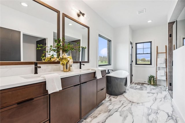 bathroom featuring recessed lighting, double vanity, marble finish floor, and a freestanding tub