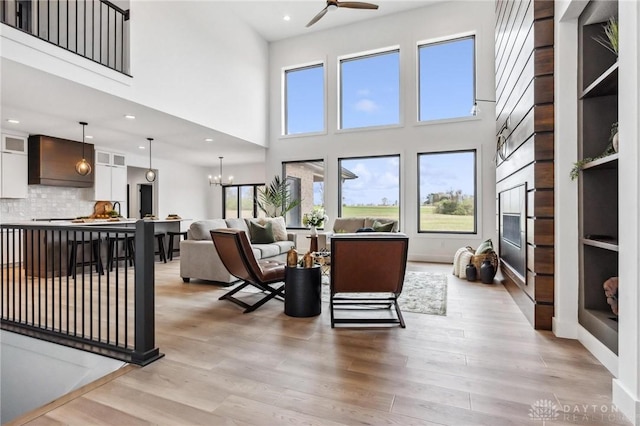 living room with a towering ceiling, recessed lighting, ceiling fan with notable chandelier, and light wood-style floors