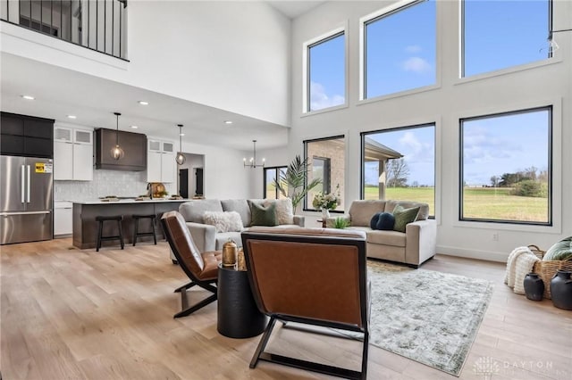 living area with light wood-type flooring, a high ceiling, and a notable chandelier