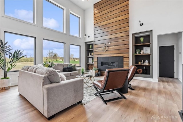living room featuring a glass covered fireplace, a high ceiling, light wood finished floors, and built in shelves