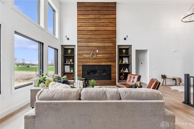living area with a glass covered fireplace, a healthy amount of sunlight, light wood finished floors, and a towering ceiling