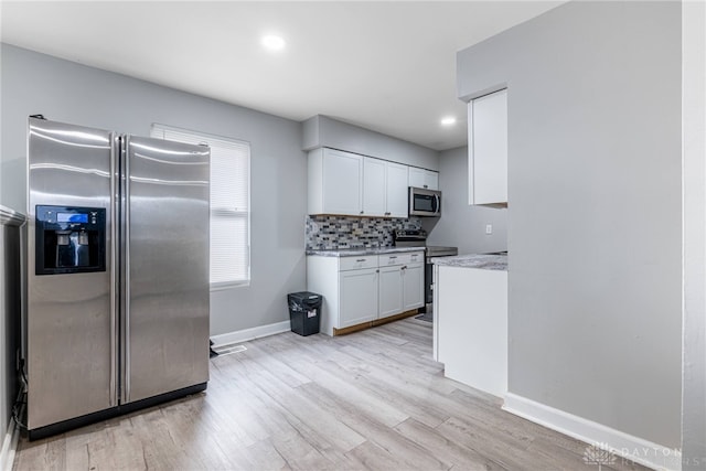 kitchen with white cabinets, decorative backsplash, light wood-type flooring, appliances with stainless steel finishes, and light stone counters