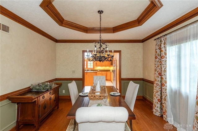 dining room featuring a raised ceiling, an inviting chandelier, light hardwood / wood-style floors, and ornamental molding