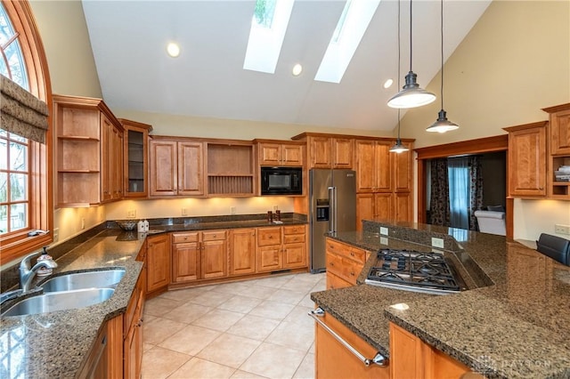 kitchen with sink, a skylight, dark stone countertops, appliances with stainless steel finishes, and decorative light fixtures