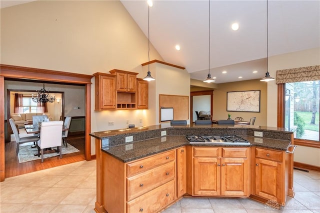 kitchen with dark stone counters, a kitchen island, hanging light fixtures, and stainless steel gas cooktop