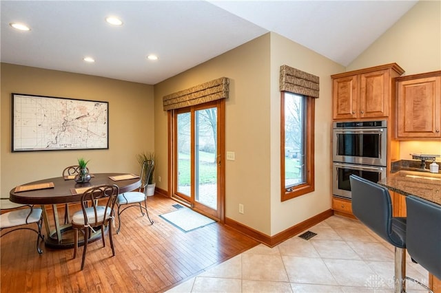 kitchen with stainless steel double oven, vaulted ceiling, dark stone counters, and light tile patterned flooring