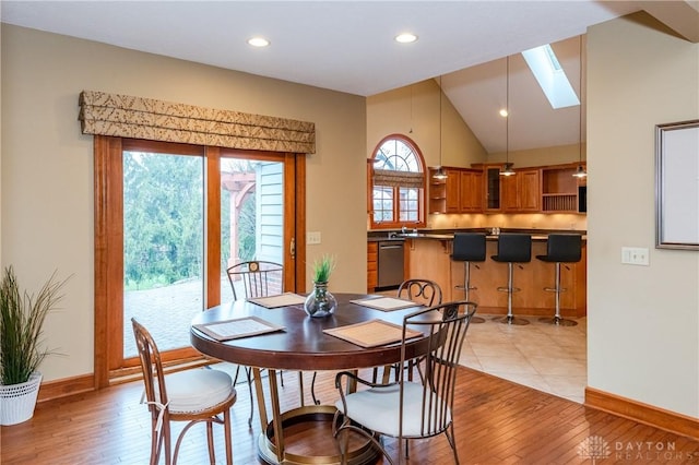 dining area featuring sink, light hardwood / wood-style flooring, and vaulted ceiling with skylight