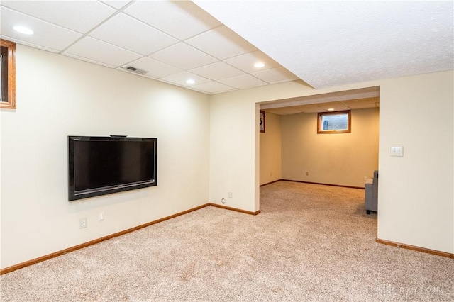 basement with a paneled ceiling and light colored carpet