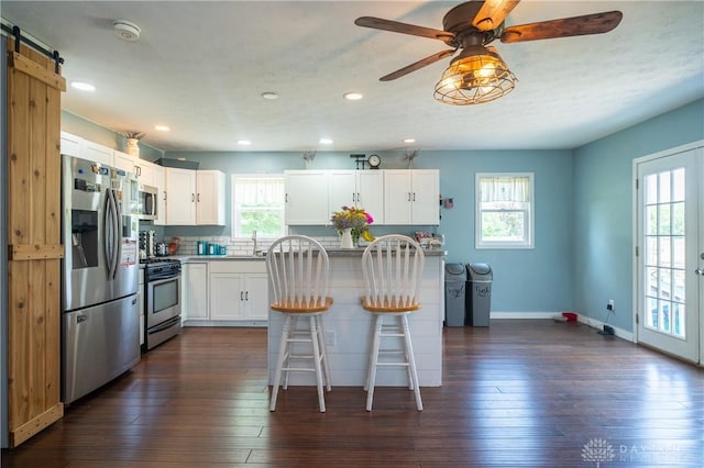 kitchen with a breakfast bar, white cabinets, sink, a barn door, and appliances with stainless steel finishes