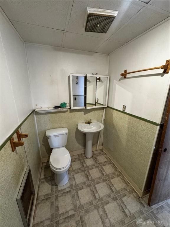 bathroom with a drop ceiling, toilet, tile walls, and sink