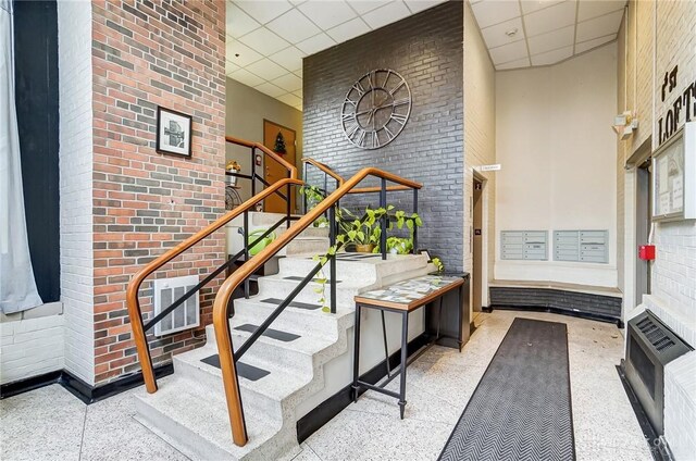 staircase featuring a paneled ceiling, a towering ceiling, and brick wall