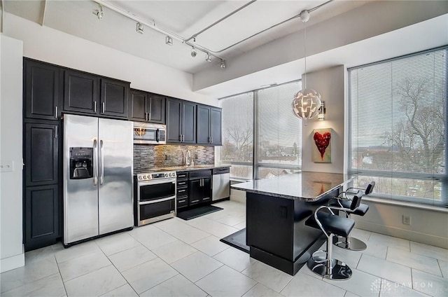 kitchen featuring rail lighting, stainless steel appliances, dark stone counters, decorative backsplash, and a breakfast bar