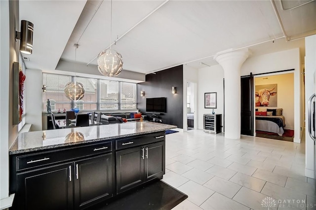 kitchen with a barn door, light stone counters, light tile patterned floors, and decorative light fixtures