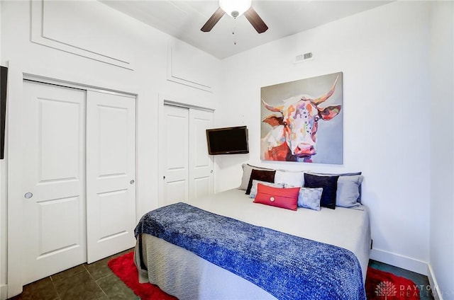 bedroom featuring ceiling fan, dark tile patterned flooring, and two closets