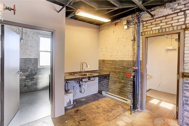 bathroom with sink, brick wall, concrete flooring, and a baseboard radiator