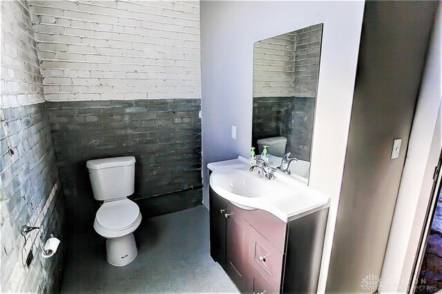 bathroom featuring vanity, toilet, concrete floors, and brick wall