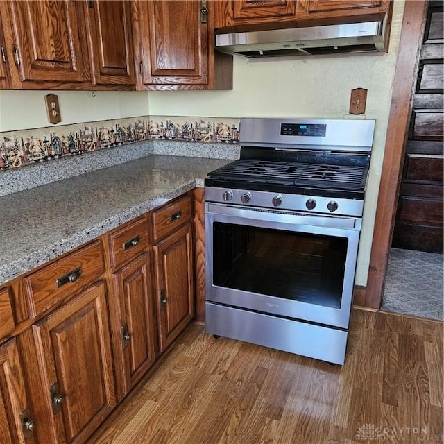 kitchen with ventilation hood, light stone countertops, stainless steel range with gas stovetop, and light wood-type flooring