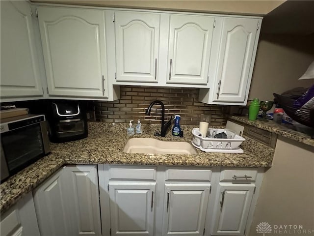 kitchen featuring decorative backsplash, white cabinetry, sink, and dark stone countertops