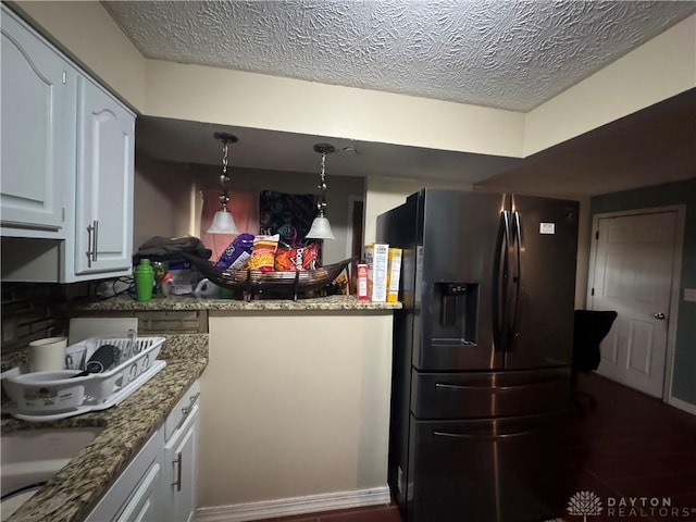 kitchen featuring dark stone counters, white cabinets, hanging light fixtures, a textured ceiling, and refrigerator with ice dispenser