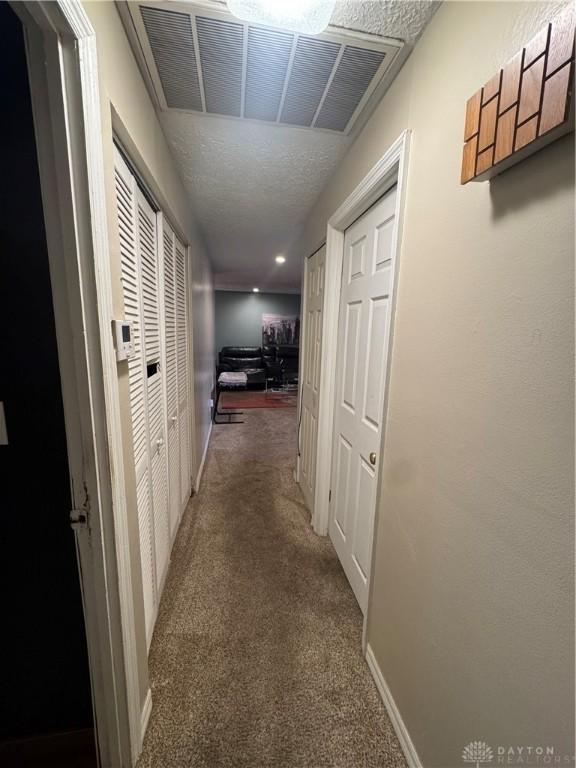 corridor with dark colored carpet and a textured ceiling