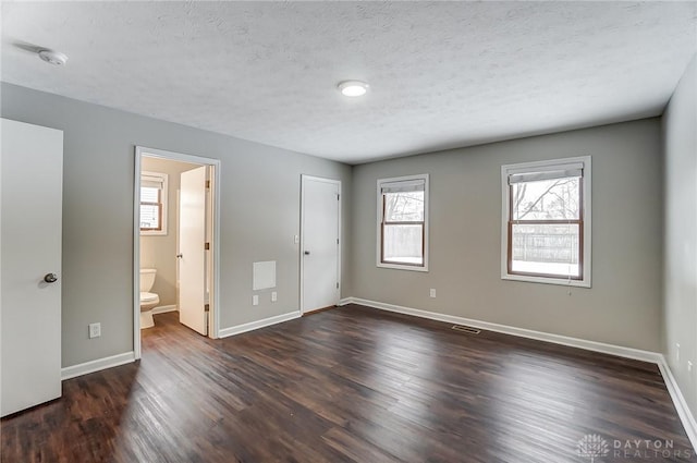 unfurnished bedroom with a textured ceiling, dark wood-type flooring, and connected bathroom