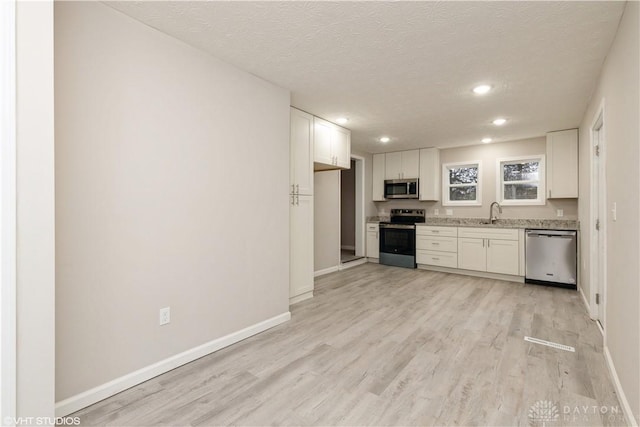 kitchen with light wood-type flooring, a textured ceiling, stainless steel appliances, sink, and white cabinetry