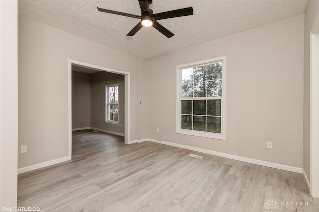 empty room with ceiling fan, light wood-type flooring, and a textured ceiling