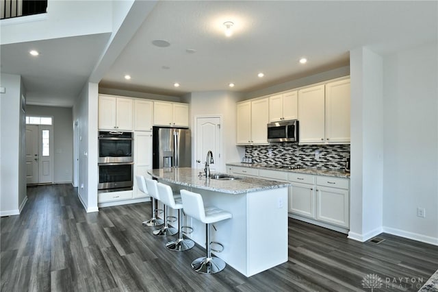 kitchen with white cabinets, sink, stainless steel appliances, and an island with sink