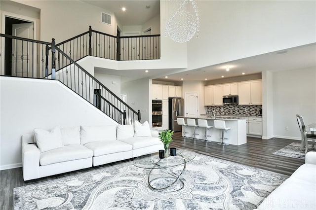 living room featuring sink, a towering ceiling, dark wood-type flooring, and a notable chandelier