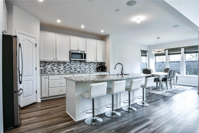 kitchen with white cabinets, hanging light fixtures, a kitchen island with sink, and appliances with stainless steel finishes