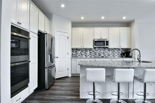 kitchen featuring white cabinets, appliances with stainless steel finishes, light stone counters, and a breakfast bar area