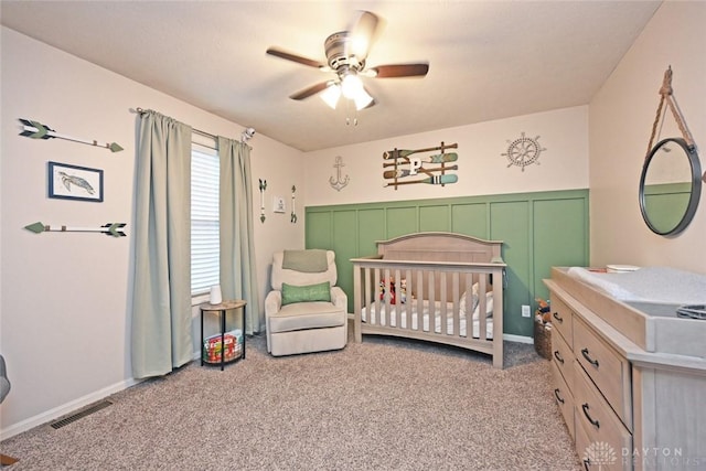 bedroom with ceiling fan, light carpet, and a nursery area